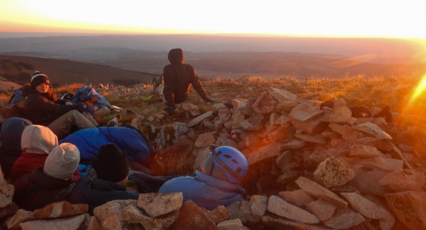 A group of people huddle at their campsite as the sunrises